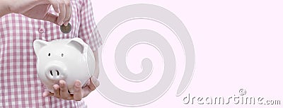Woman putting coins in piggy bank. Female holding pink piggy bank isolated. Money bank in female hand on pink background Stock Photo
