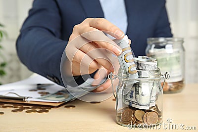 Woman putting dollar bill into jar with money on table, closeup Stock Photo