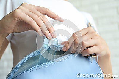 Woman putting hand sanitizer in purse on light background, closeup. Personal hygiene during COVID-19 pandemic Stock Photo