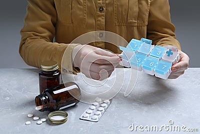 Woman putting pill into weekly organizer at grey marble table, closeup Stock Photo