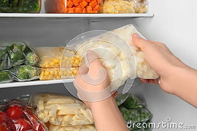 Woman putting plastic bag with cauliflower in refrigerator with frozen vegetables Stock Photo