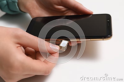 Woman putting SIM card tray in smartphone at white table, closeup Stock Photo