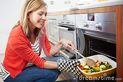 Woman Putting Tray Of Roast Vegetables Into Oven Stock Photo