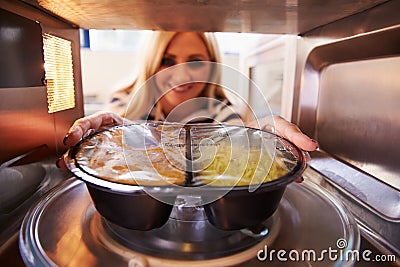 Woman Putting TV Dinner Into Microwave Oven To Cook Stock Photo