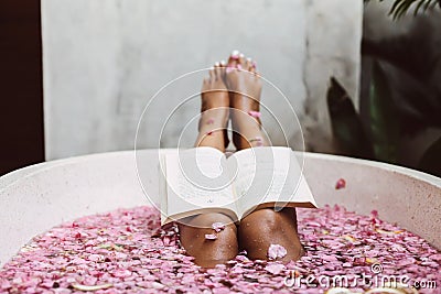 Woman reading book while relaxing in bath tub with flower petals Stock Photo