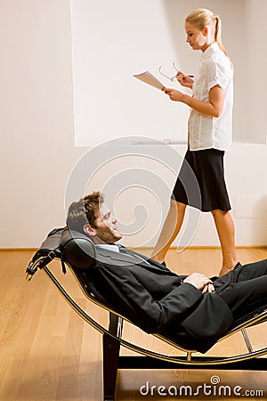 Woman reading man lying on chaise longue Stock Photo