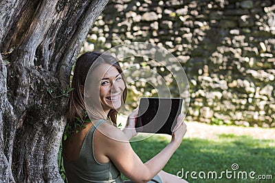 Woman reading tablet and enjoy rest in a park under tree Stock Photo