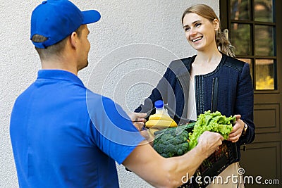 Woman receive online grocery order box from delivery man at home Stock Photo