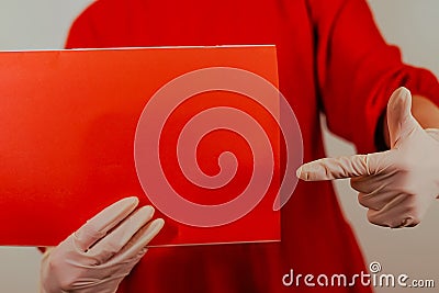 Woman on a red background in medical gloves holds a red poster. Close-up Stock Photo