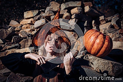 Woman with red blood and with blond hair. Scary bloody girl in wizard orange hat with pumpkin. Halloween party art Stock Photo