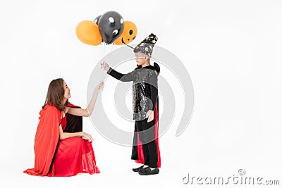 Woman in red costume giving fancy balloons to kid boy in back suit on white background. Concept for funny playing in halloween fe Stock Photo