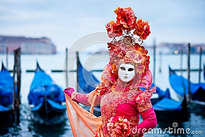 Woman in red dress masked for Venice Carnival in front of typical gondola boats Stock Photo