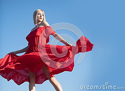 Woman in red dress movement on sky. Stylish fashion woman posing outdoor. Attractive young woman in sexy dress enjoying Stock Photo