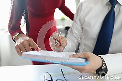 Woman in red dress show finger and man in shirt and tie hold notebook and write in office. Stock Photo