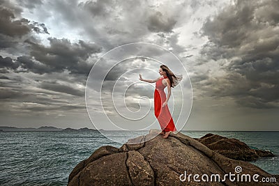 Woman in red dress stands on a cliff with a beautiful sea view a Stock Photo