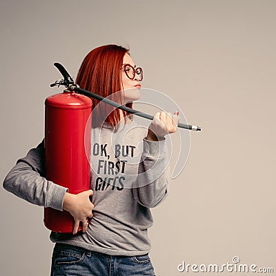 A woman with red hair in the Studio holding a fire extinguisher. An emotional bright woman extinguishes everything with Stock Photo