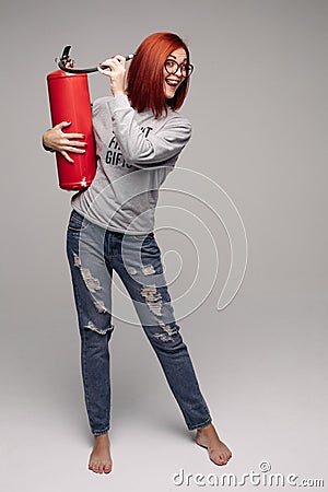 A woman with red hair in the Studio holding a fire extinguisher. An emotional bright woman extinguishes everything with Stock Photo