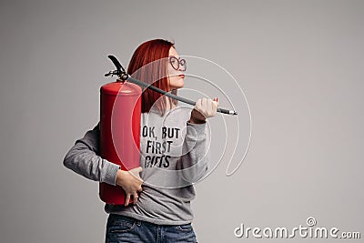 A woman with red hair in the Studio holding a fire extinguisher. An emotional bright woman extinguishes everything with Stock Photo