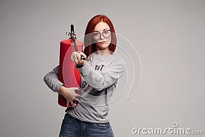 A woman with red hair in the Studio holding a fire extinguisher. An emotional bright woman extinguishes everything with Stock Photo