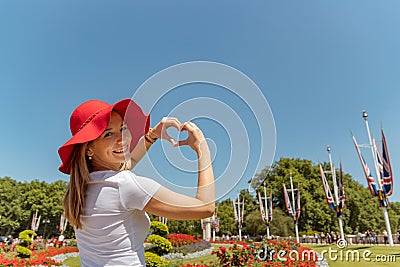 Woman with red hat frames flowers into heart shape, finger heart frame. looking and smiling to the camera Stock Photo