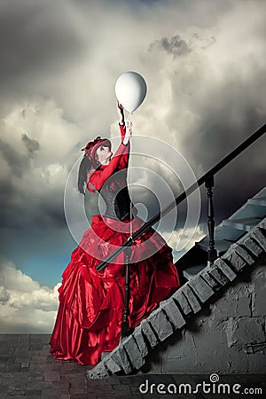 Woman in a red historical dress is catching a white balloon. Stock Photo