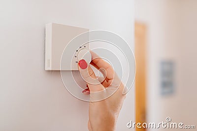 Woman regulating temperature on home heating thermostat Stock Photo