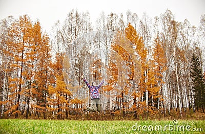 Woman rejoices at the arrival of autumn. Girl in a field near the yellow autumn forest, autumn came, the emotion of joy Stock Photo