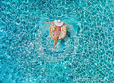 Woman relaxes on a donut shaped float over blue, sparkling pool water Stock Photo