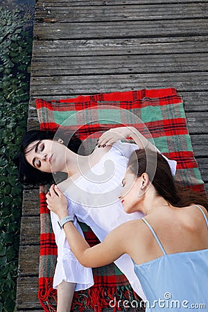 Two teenager girls sitting on a pier at the river bank having good time in summer. happy girl friends relaxing outdoor near lake. Stock Photo