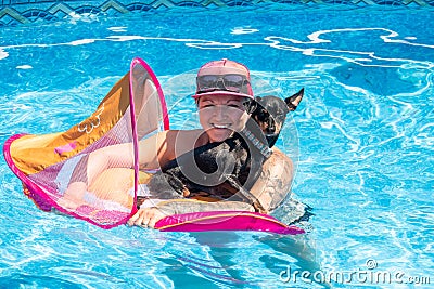 Woman relaxing with black pinscher dog on a flotation device in the swimming pool Stock Photo