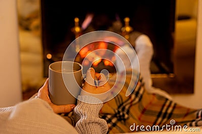 Woman relaxing by the fireplace warming up feet in woolen with a cup of hot drink socks and blanket Stock Photo