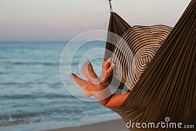 Woman relaxing on hammock with hat sunbathing on vacation. Against the background of the sea in the setting sun. Stock Photo