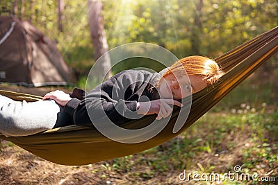 Woman relaxing in the hammock in the middle of a pine forest, watching sundown. Slow life concept. Hipster. Camping tent. Close-up Stock Photo