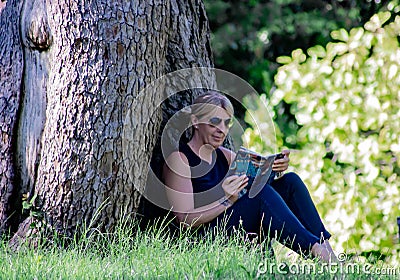 Woman relaxing in a park reading, mature blonde. for many, reading is a way to rest from stress, but it is also very healthy becau Stock Photo