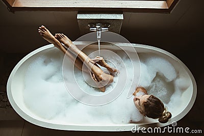 Woman relaxing in foam bath with bubbles in dark bathroom by window Stock Photo