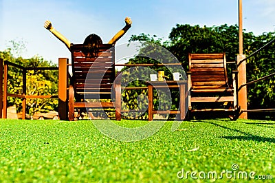 Woman relaxing on wooden sunbed on green artificial grass and looking the blue sky Stock Photo