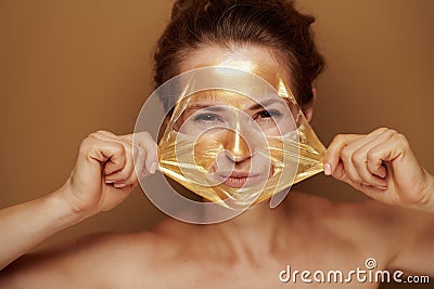 Woman removing golden mask on brown background Stock Photo