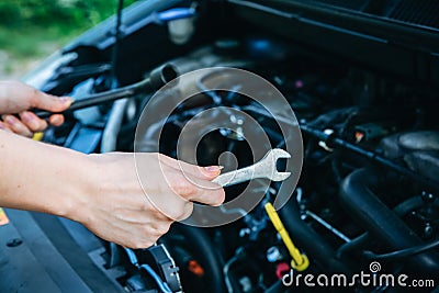 Woman is repairing broken car. Accident situation while travelling. Opened bonnet of vehicle. Girl is holding instruments for Stock Photo