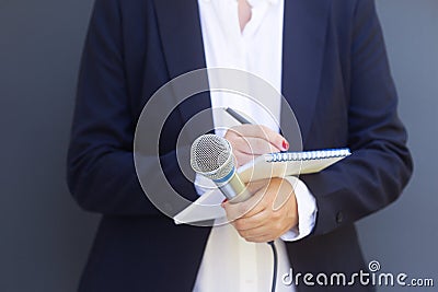Woman reporter or journalist at media event, holding microphone, writing notes. Broadcast journalism concept. Stock Photo