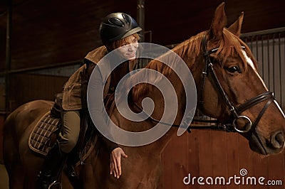 Woman rider in saddle praises bay horse affectionately patting neck Stock Photo