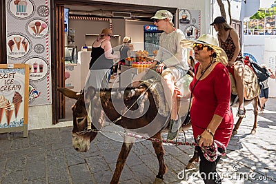 Woman riding donkey. Using donkey taxi to the Acropolis is a popular tourist attraction in Lindos Editorial Stock Photo