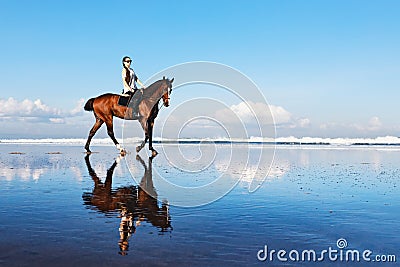 Woman riding horse on beach along sea by water pool Stock Photo