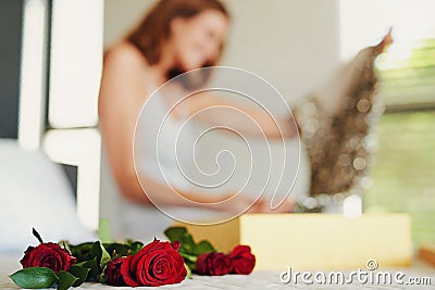 Woman, roses and box with gift in bedroom on birthday, celebration and valentines day event in home. Girl, dress and Stock Photo