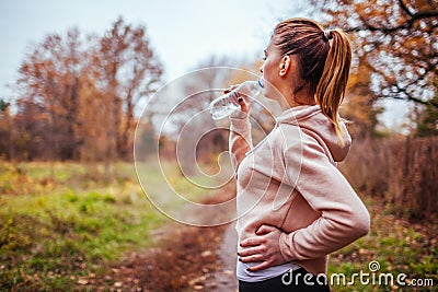 Woman runner drinks water in autumn forest Stock Photo