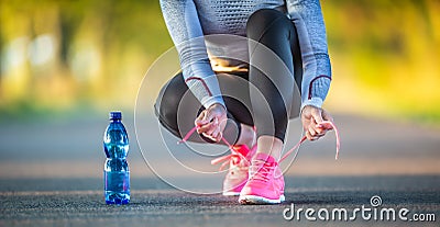 Woman runner tying shoelaces before jogging in autumn tree alley park. Sports female autumn outfit leggings and thermal underwear Stock Photo