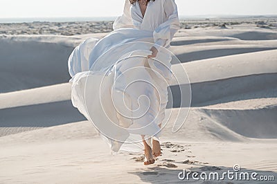 Woman running barefoot in desert in beautiful flowing bridal white dress Stock Photo