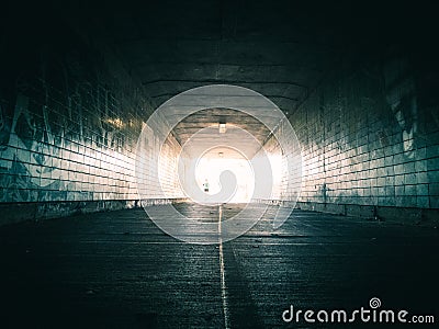 Woman running through tunnel towards bright light Stock Photo