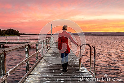 Woman on rustic timber jetty watching beautiful sunset Stock Photo