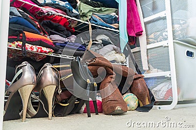 Woman`s closet with high heel shoes, stacked, folded clothes on shelves and part of robes hanging. Depicting closet organization, Stock Photo