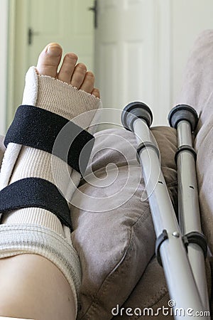 Woman`s foot which is injured and is wearing a brace and crutches Stock Photo